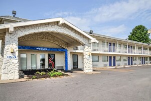 A motel with a stone facade, a 'Welcome' sign, and multiple rooms with blue doors.