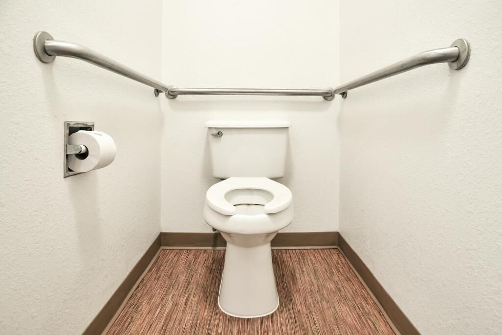 Een badkamer met een wit toilet, toiletpapier en een handgreep.
