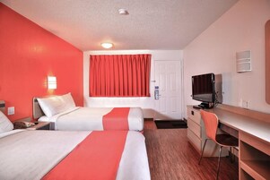 A hotel room with two beds, a desk, a television, and a door.