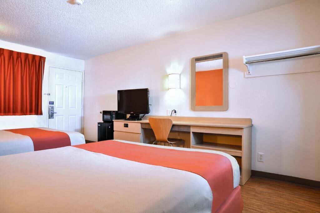 A hotel room with two beds, a desk, a chair, a television, and a mirror.