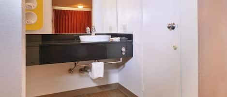 A bathroom with a black countertop, white sink, and a mirror. There is a towel rack with rolled towels and a red curtain in the background.
