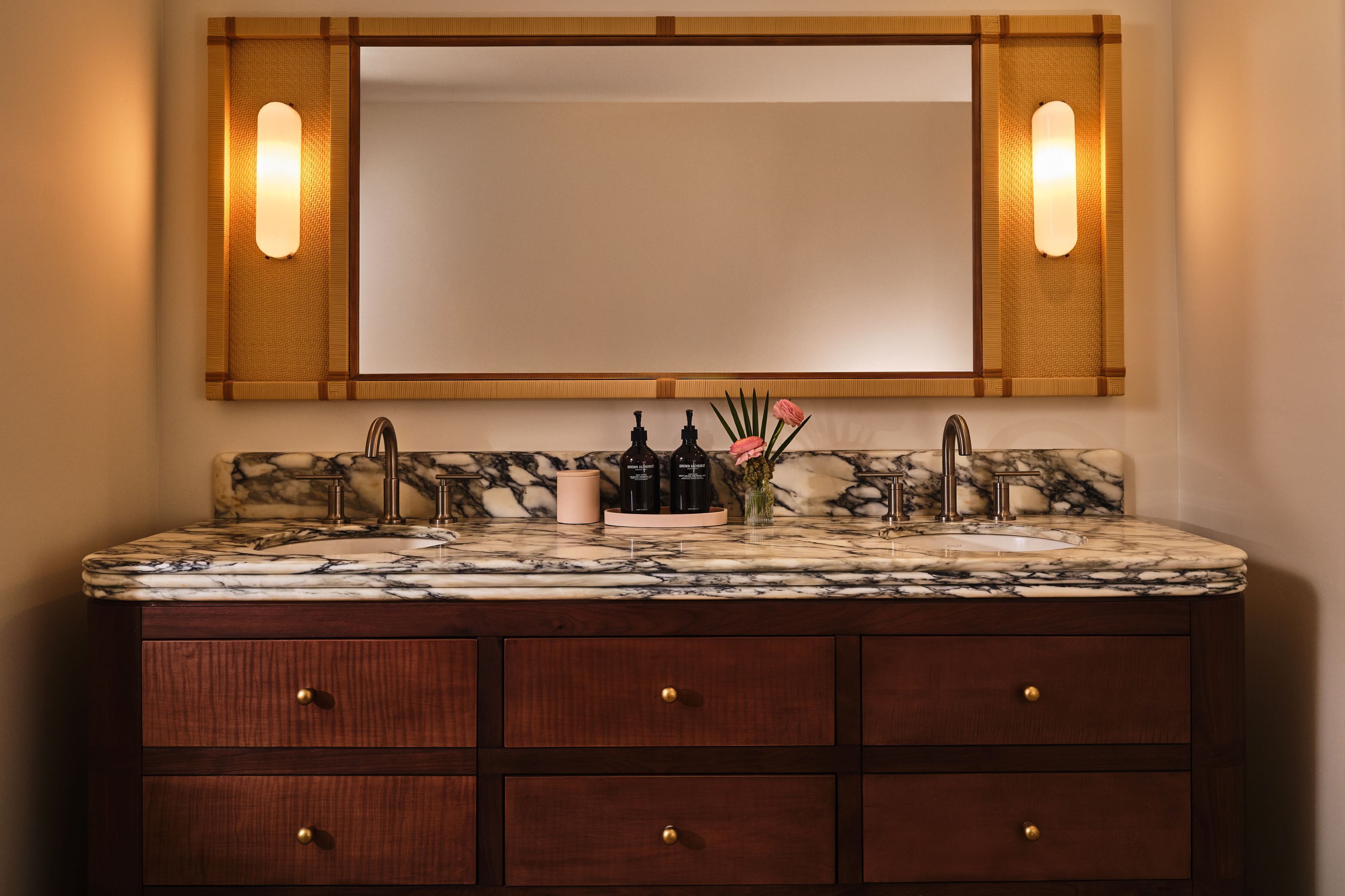 A bathroom vanity with a marble countertop, two faucets, and a mirror above.