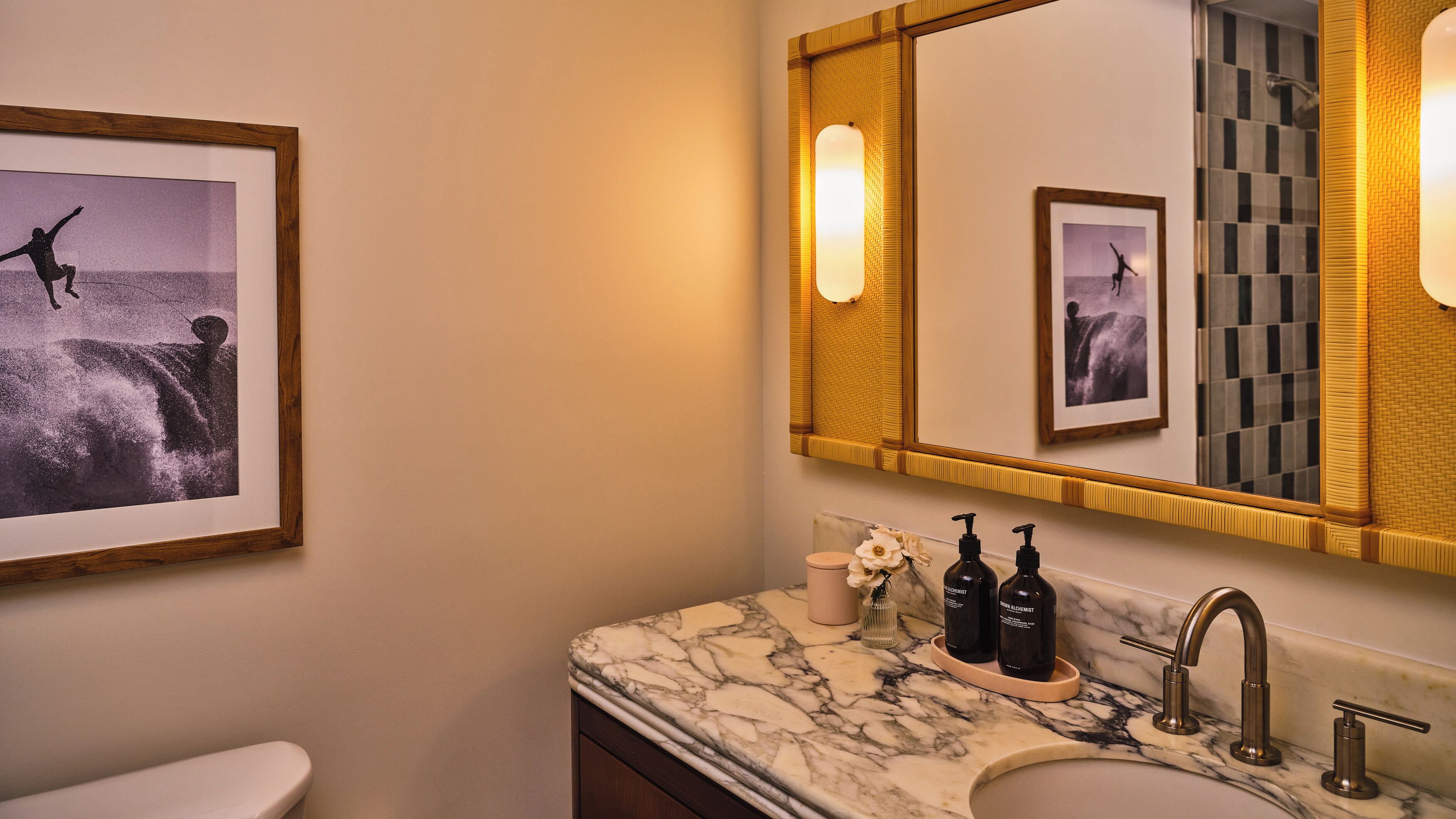 Een badkamer met een marmeren wastafel, twee zwarte zeepdispensers, een toilet en ingelijste foto's aan de muur.