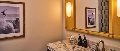 A bathroom with a marble sink, two black soap dispensers, a toilet, and framed pictures on the wall.