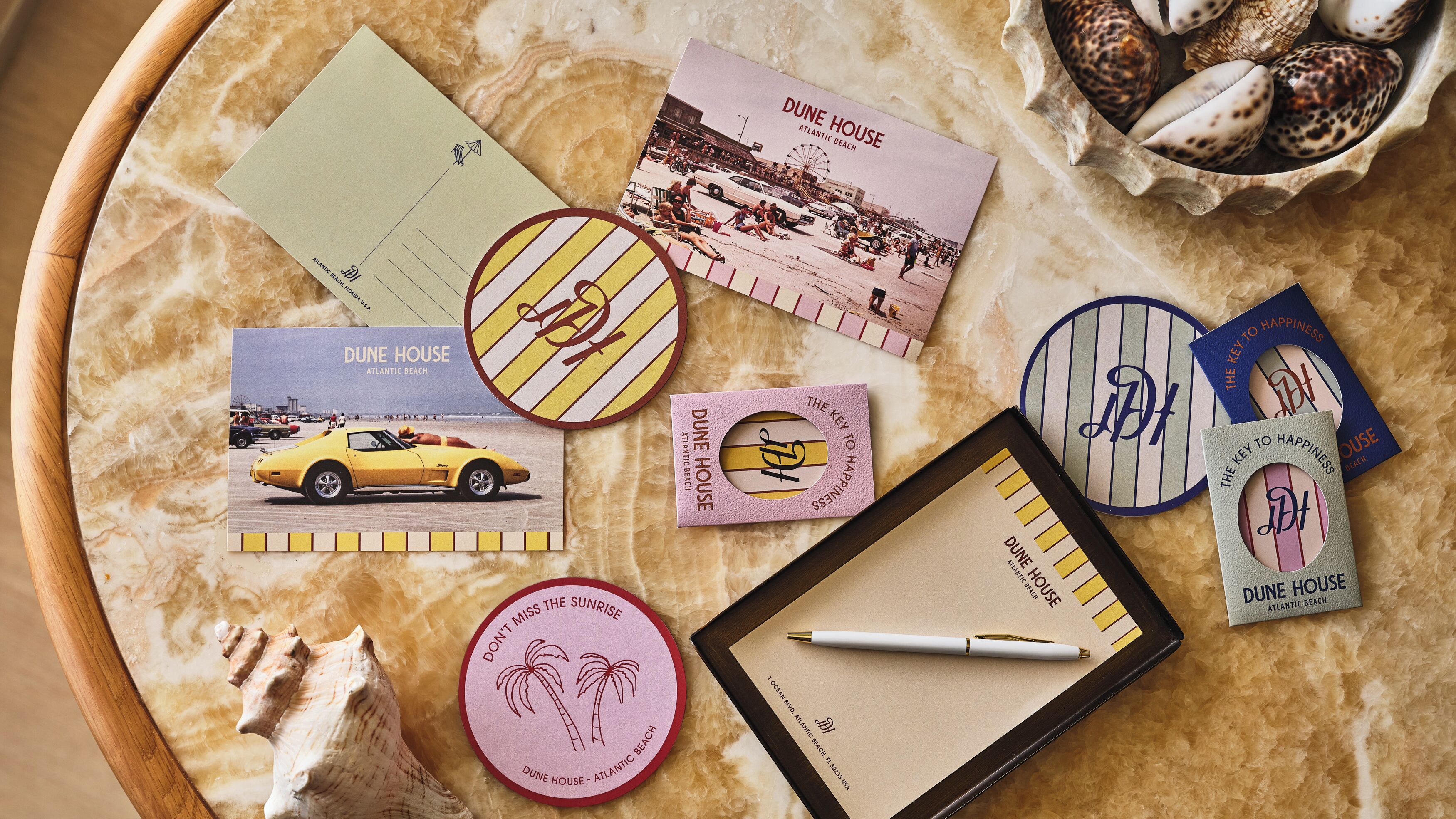 Variedad de artículos de papelería, incluyendo postales, un cuaderno, un bolígrafo y platos decorativos con texto e imágenes, todo sobre una superficie texturizada.