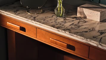 A bathroom vanity with a marble countertop, a glass vase with red flowers, and a round stool.