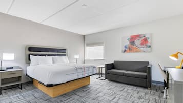 A modern hotel room with a bed, a sofa, a desk, and a lamp.