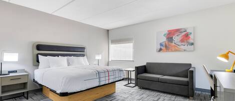 Una habitación de hotel moderna con cama, sofá, escritorio y lámpara.