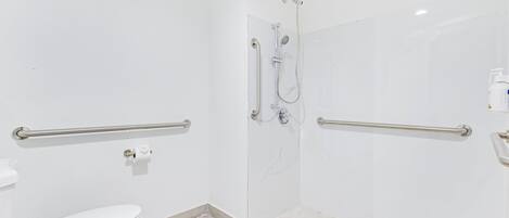Un baño con inodoro, ducha con barras de apoyo y suelo de azulejos blancos.