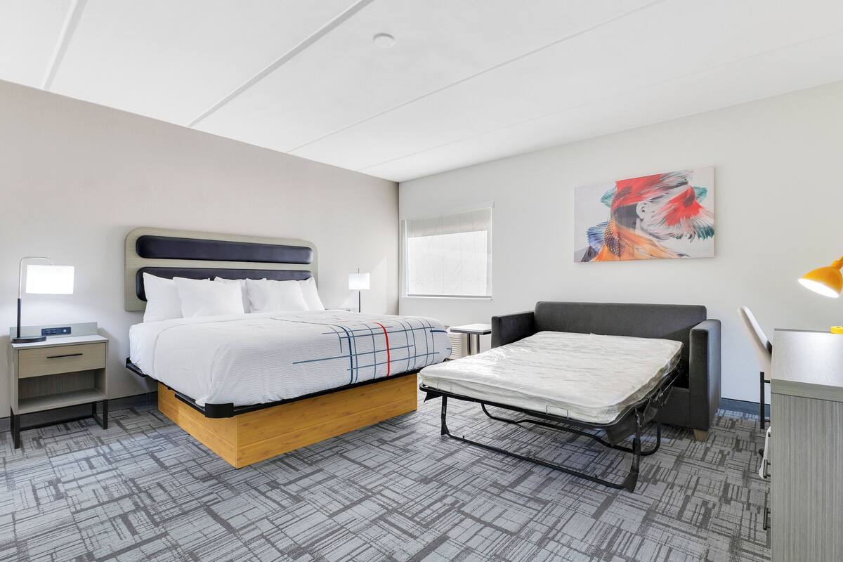 A modern hotel room with a bed, a desk, a chair, and a small table.