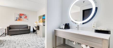 Une salle de bain moderne avec un miroir rond, un lavabo blanc et un espace pour ranger les serviettes.