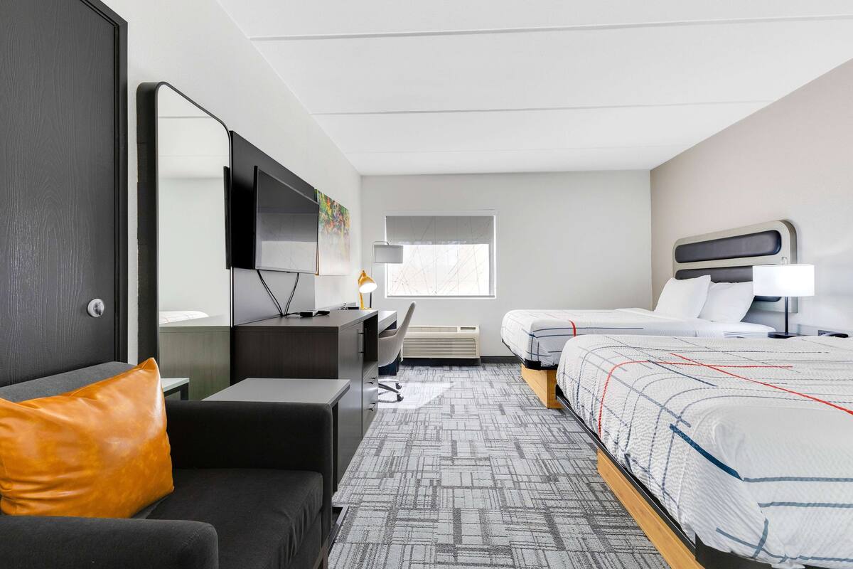 A hotel room with a bed, a desk, a chair, a sofa, a TV, and a window.