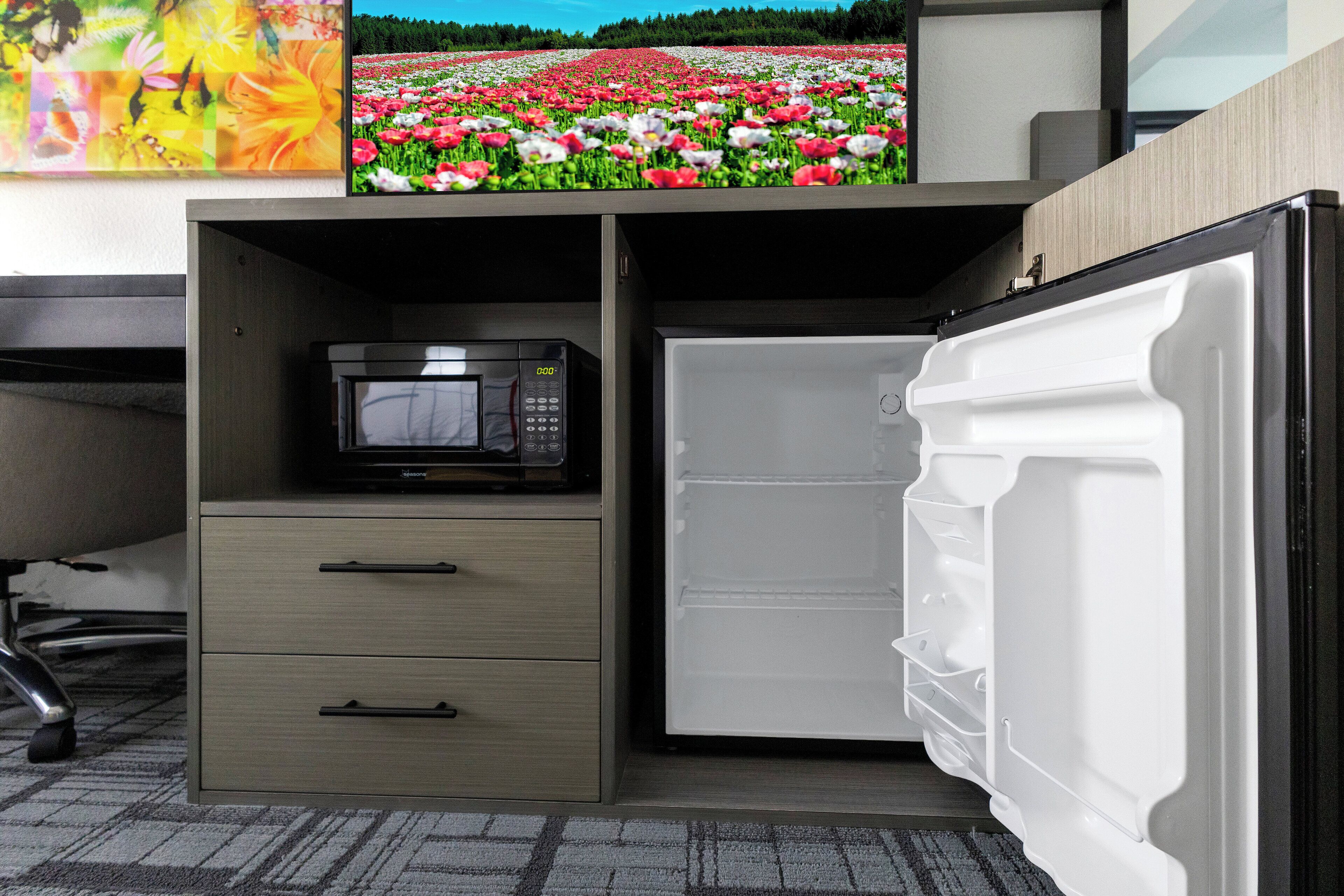 Una kitchenette compacta con microondas, refrigerador y un pequeño mueble cajonero.