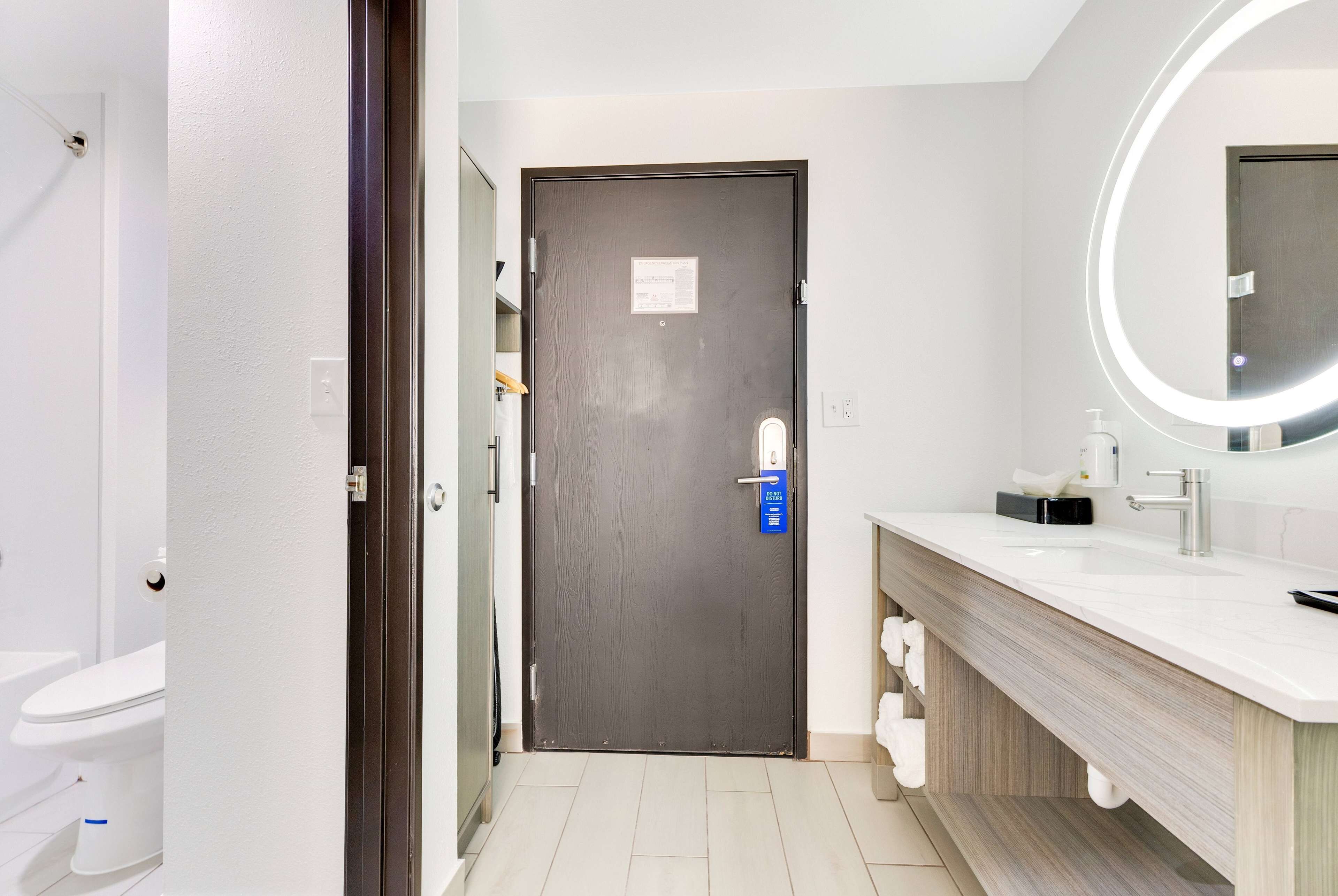 Un baño moderno con una puerta oscura, un lavabo blanco con espejo, y un inodoro visible al fondo.