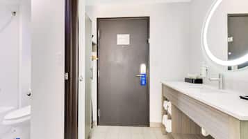 Un baño moderno con una puerta oscura, un lavabo blanco con espejo, y un inodoro visible al fondo.