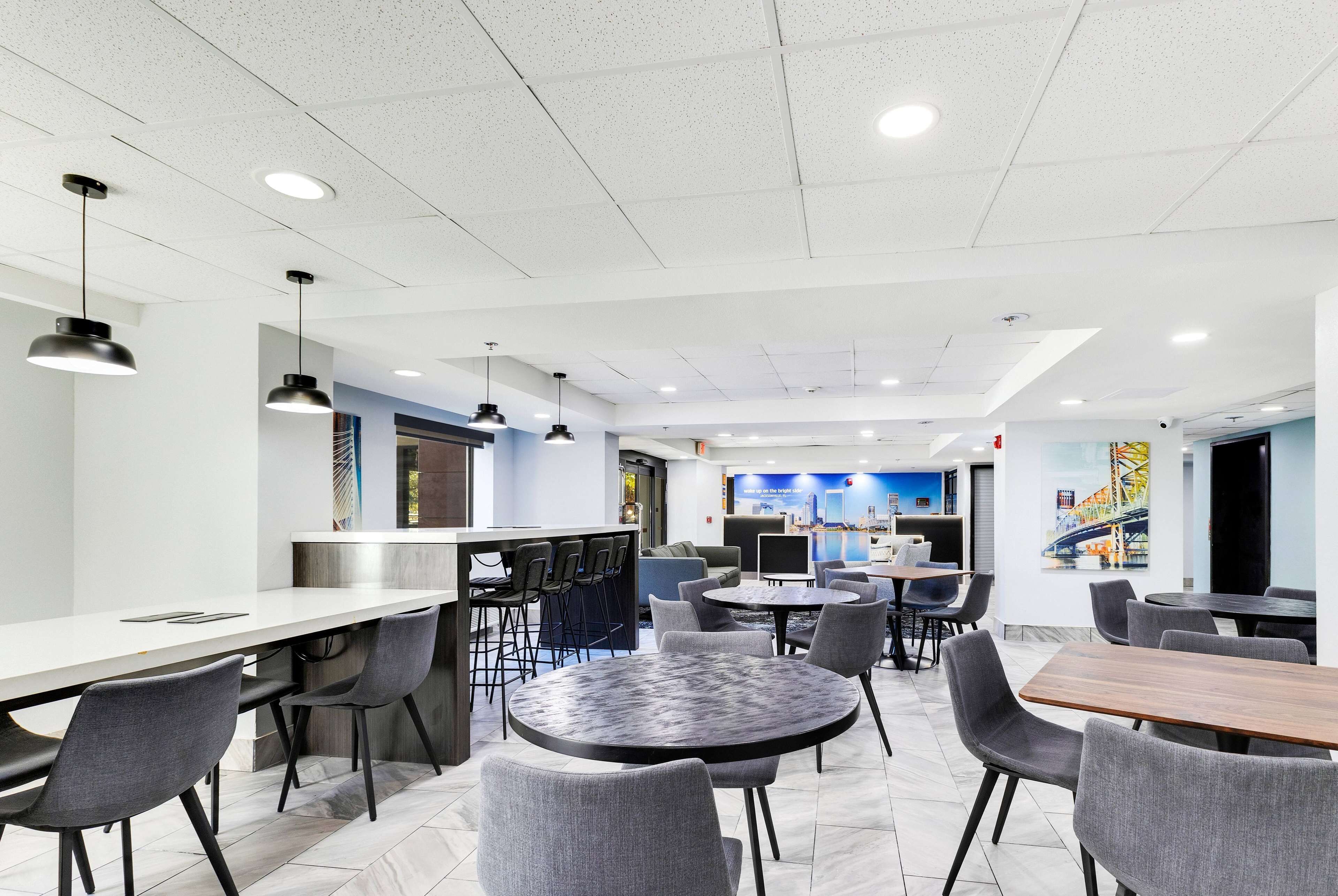 A modern dining area with bar seating, round tables, and grey chairs.