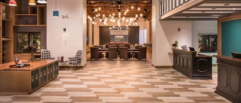 Un vestíbulo espacioso con piso de madera en serpeto, una zona de estar central con una mesa grande y una escalera que conduce a un nivel superior.