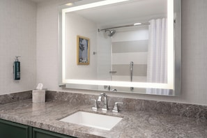 Un baño con un espejo grande, un lavamanos y una ducha.