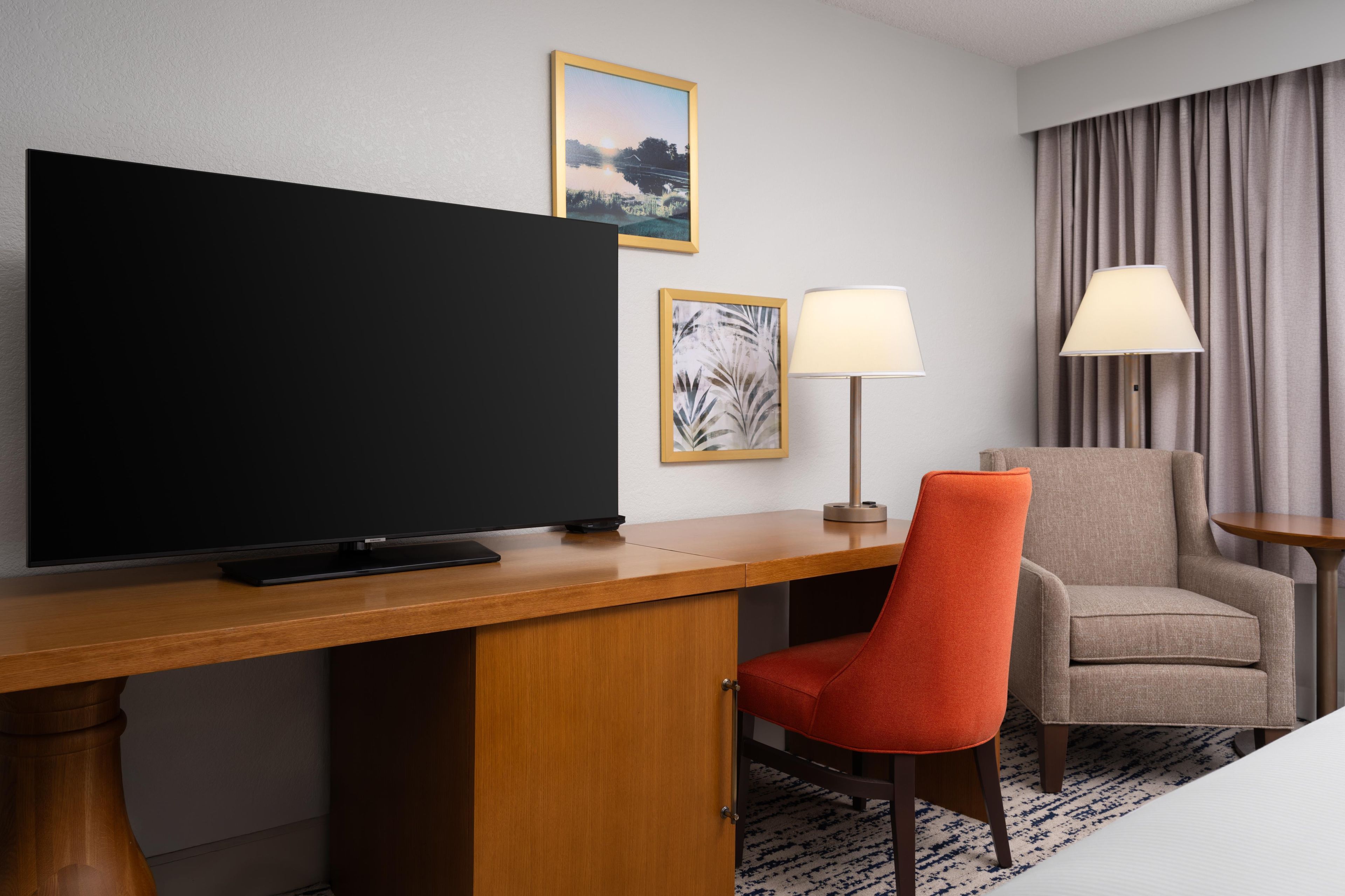 Habitación de hotel con televisión de pantalla plana, escritorio con lámpara, una silla y un sofá.