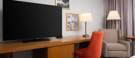 Een hotelkamer met een flatscreen televisie, een bureau met lamp, een stoel en een bank.