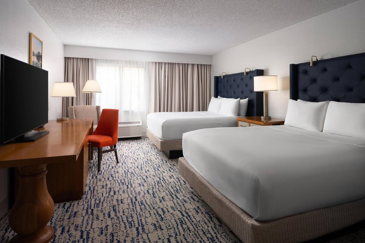 A hotel room with two beds, a desk, a chair, and a television.