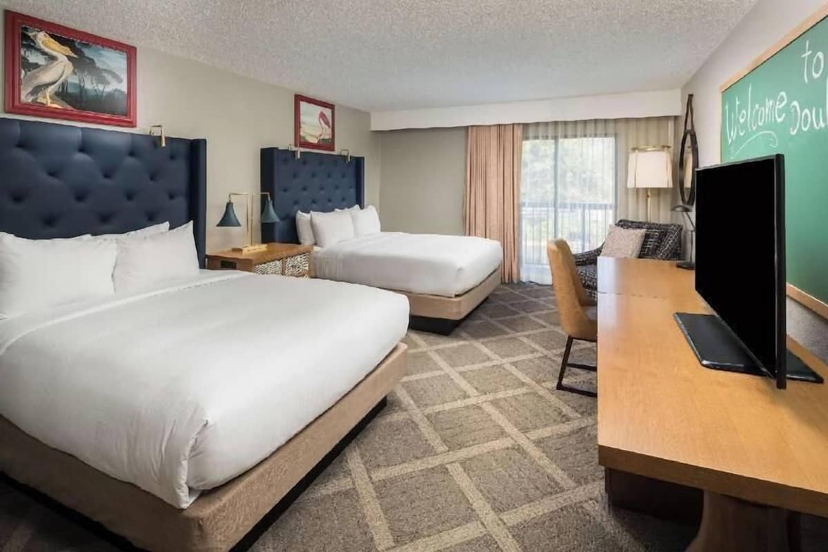 A hotel room with two beds, a desk, a television, and a chalkboard with 'Welcome to DoubleTree' written on it.