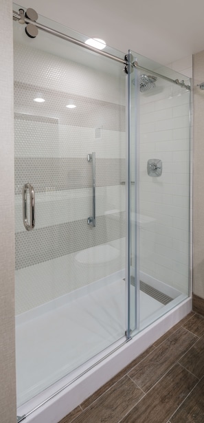 Ducha con mampara de vidrio, pared de azulejos y un tirador metálico.