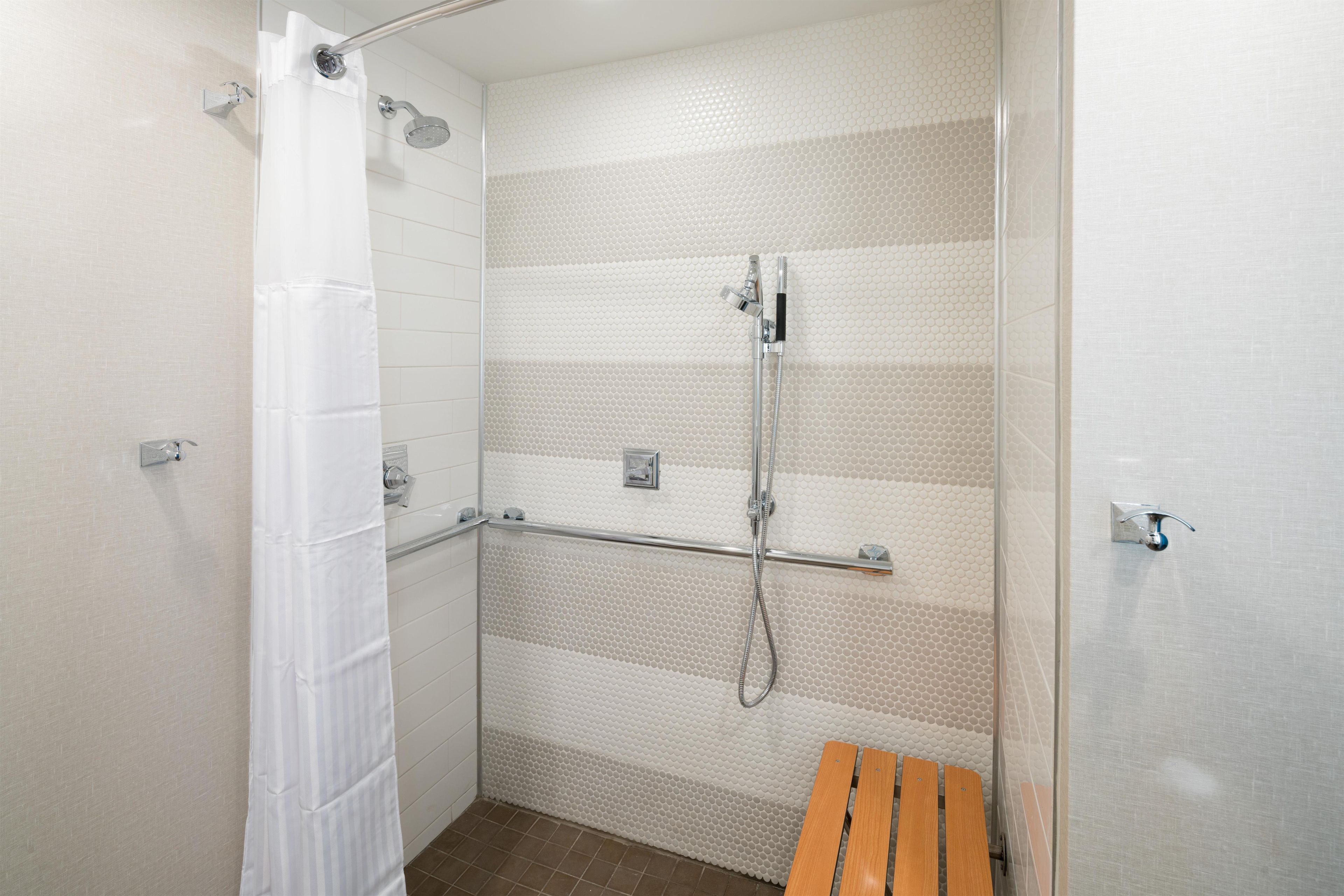 A shower area with a glass door, a showerhead, and a bench.
