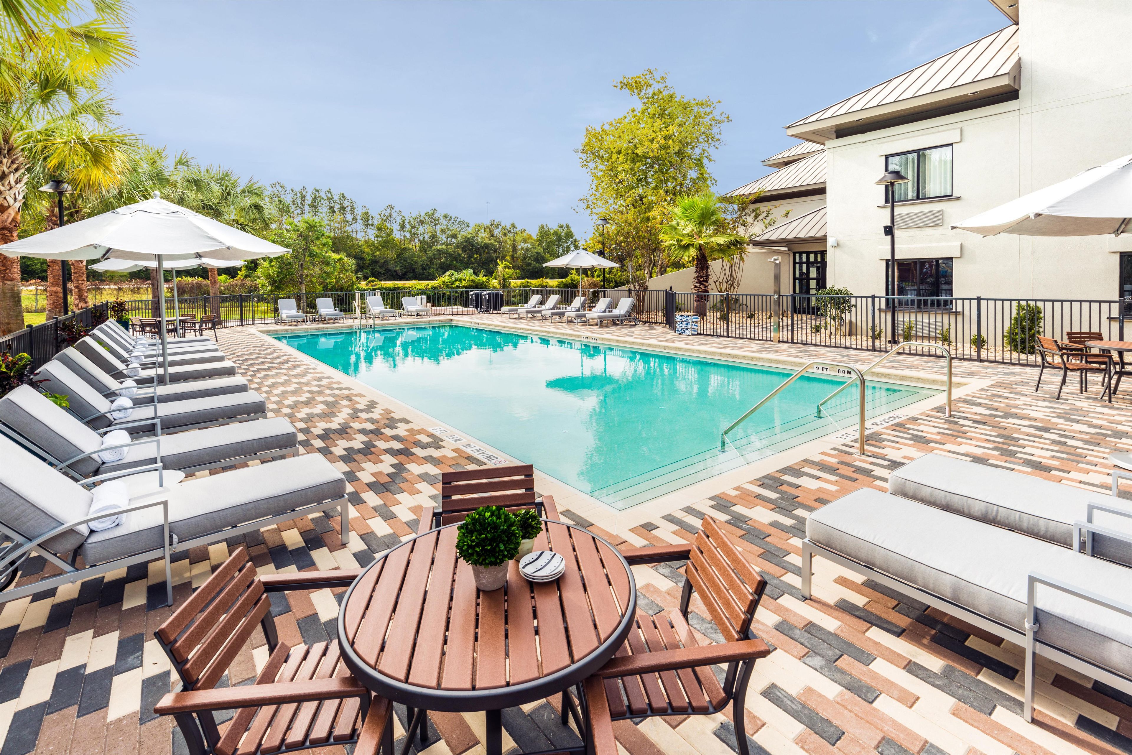 Une piscine entourée d’un espace extérieur pavé à motifs, agrémenté de chaises longues et de parasols.
