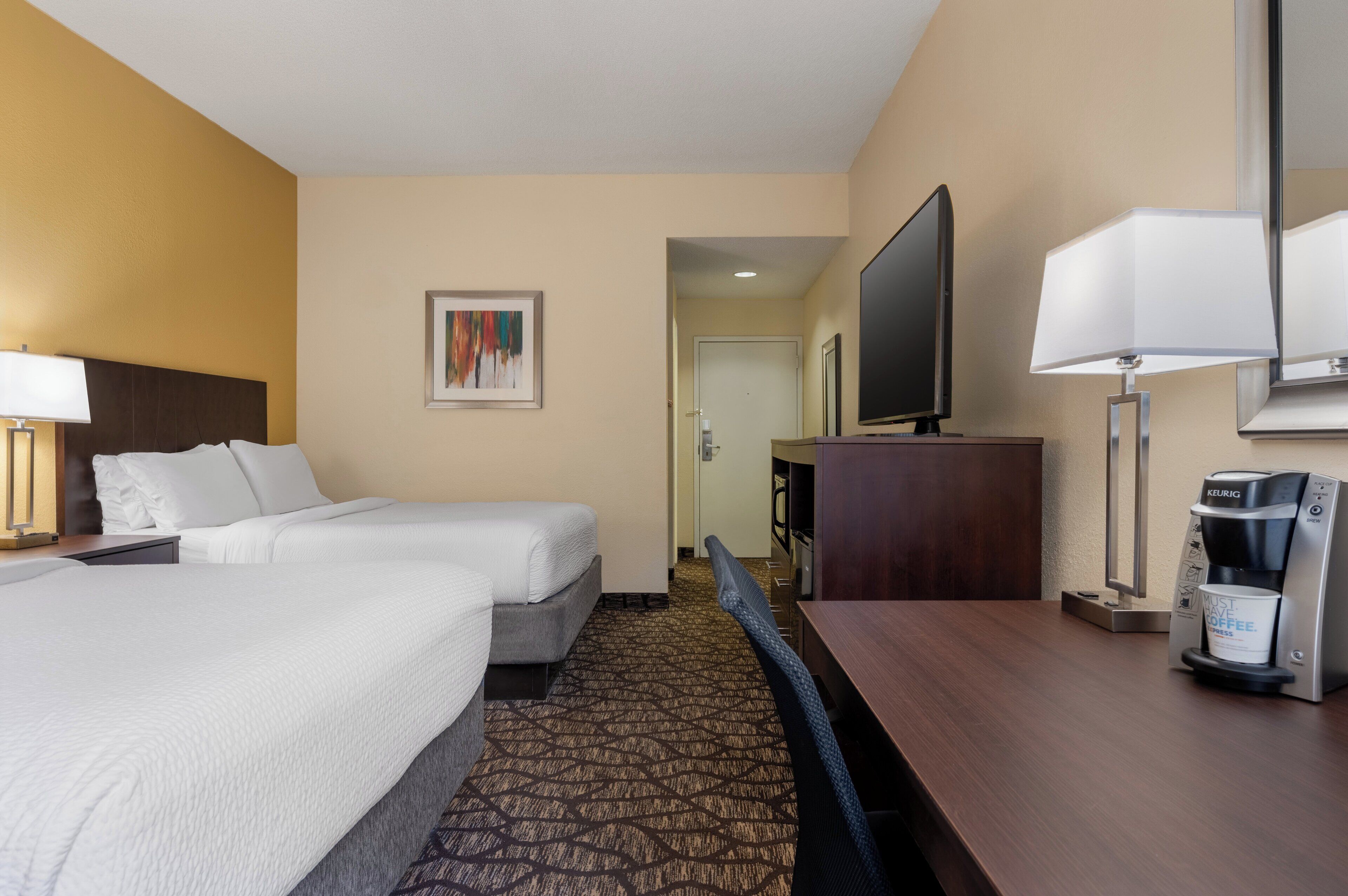 A hotel room with two beds, a television, a coffee maker, and a desk.