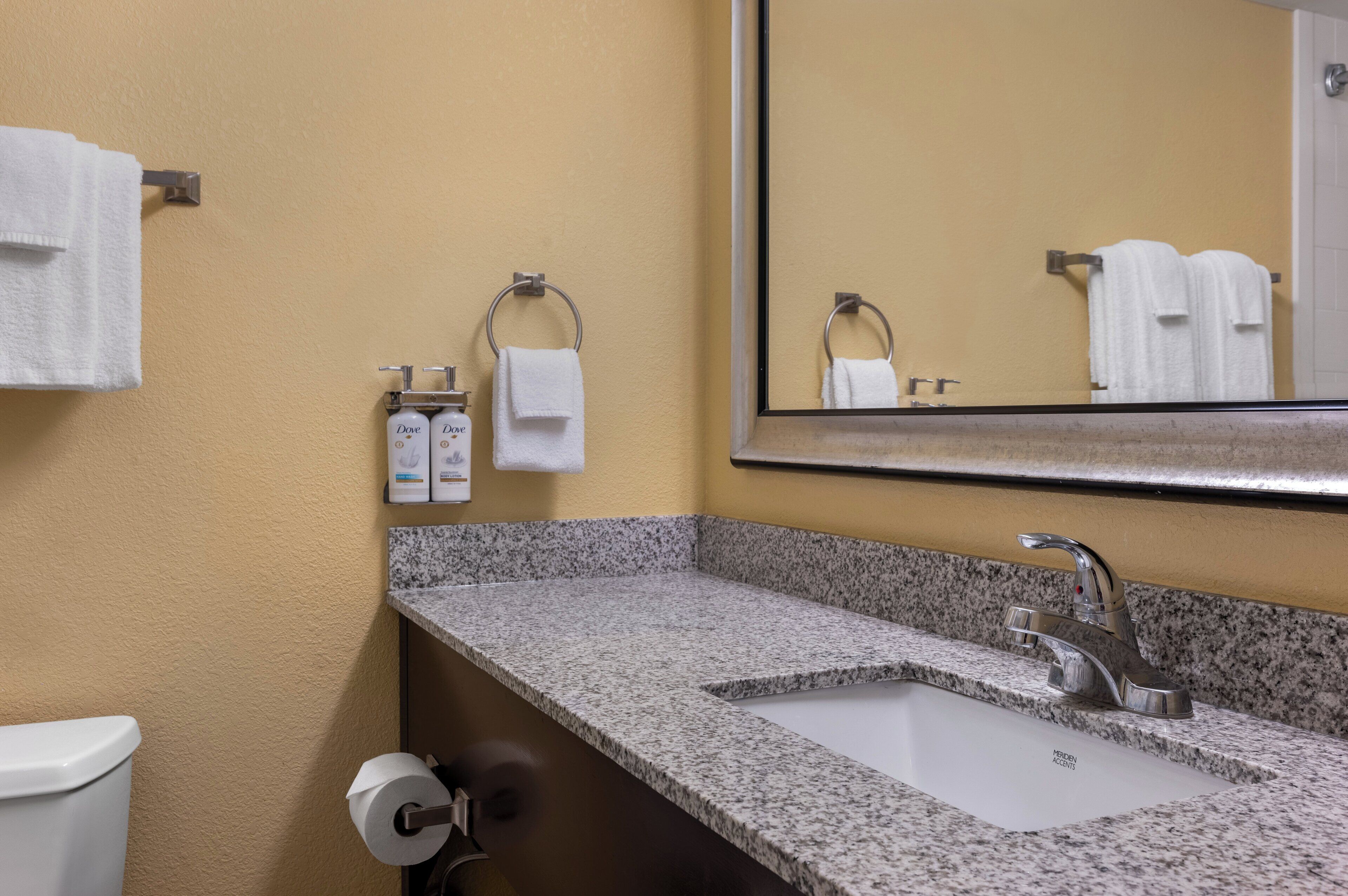 Une salle de bain avec un lavabo doté d’un plan de travail en granit, un miroir et deux serviettes blanches suspendues à des porte-serviettes en métal.