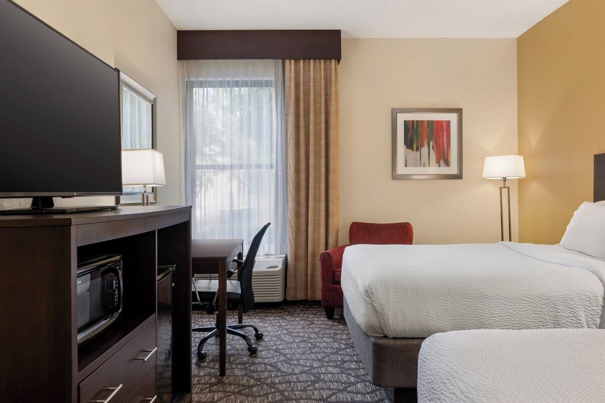 A hotel room with a bed, a desk with a chair, a television, a microwave, and a painting on the wall.