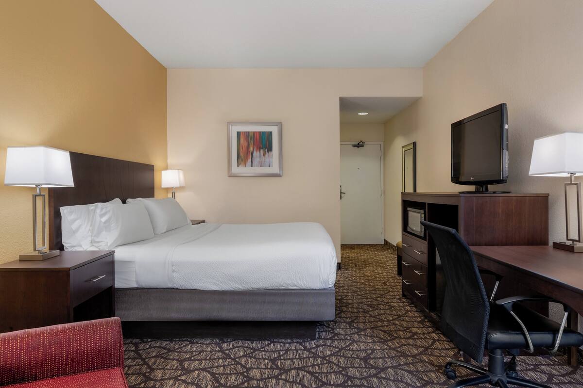 A hotel room with a bed, desk, chair, television, and artwork on the wall.