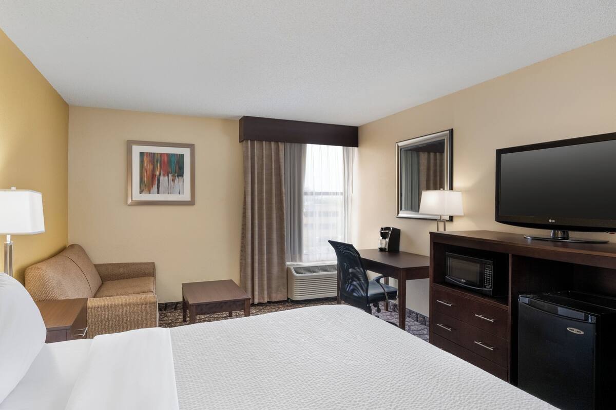 A hotel room with a bed, a desk with a computer, a chair, a television, and a microwave.