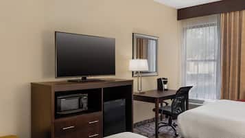 Quarto de hotel com TV de tela plana, escrivaninha com luminária, micro-ondas, geladeira, uma cadeira e duas camas.