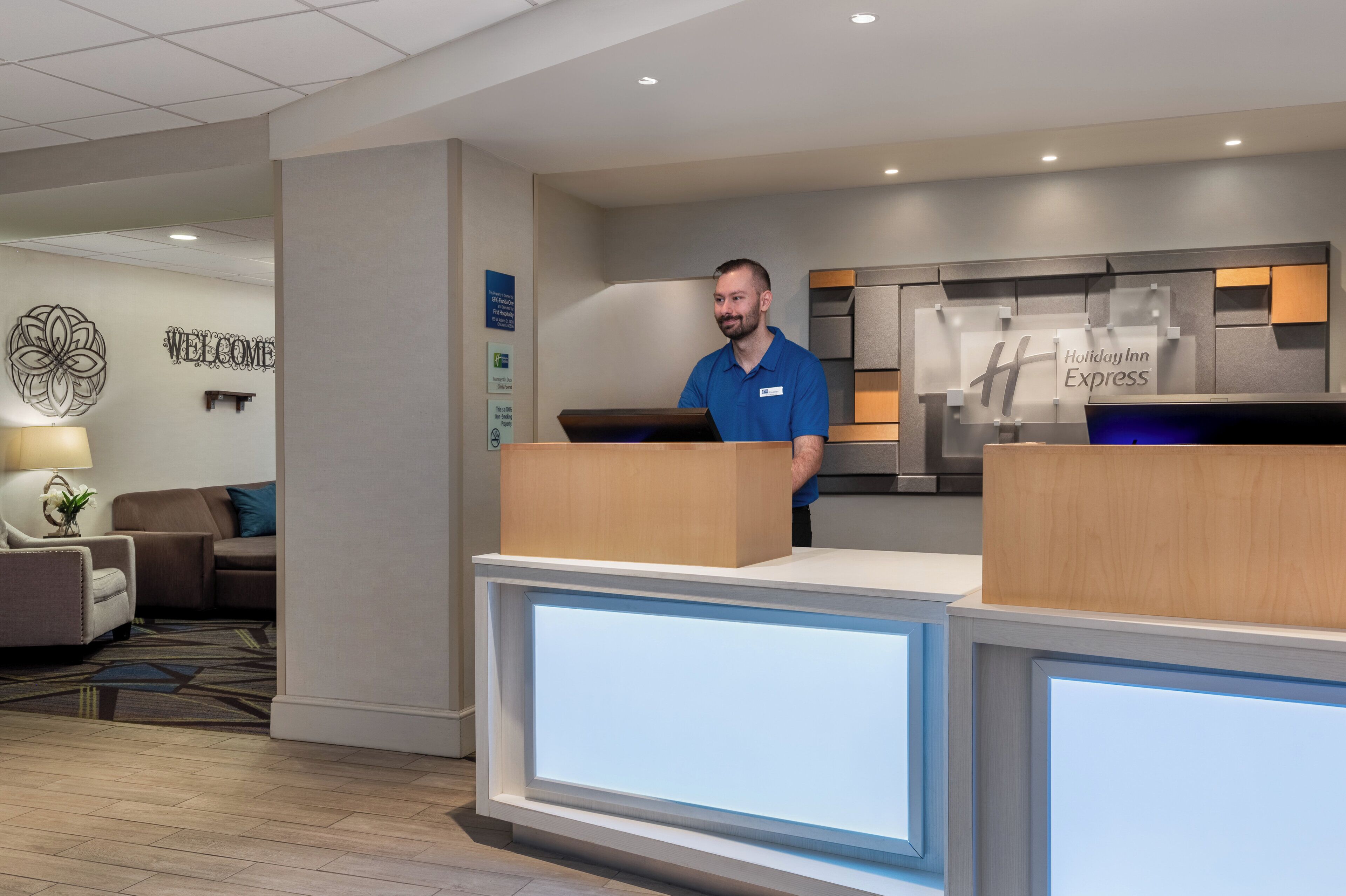 A Holiday Inn Express reception area with a modern design, including a reception desk, a 'Welcome' sign, and a 'Holiday Inn Express' sign.