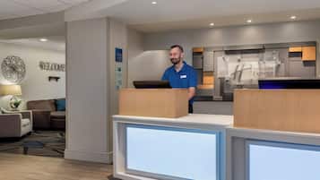 Ein Empfangsbereich eines Holiday Inn Express mit modernem Design, inklusive einer Rezeption, einem 'Welcome'-Schild und einem 'Holiday Inn Express'-Schild.