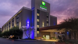 A Holiday Inn Express building with a prominent green logo, large windows, and a well-lit entrance.