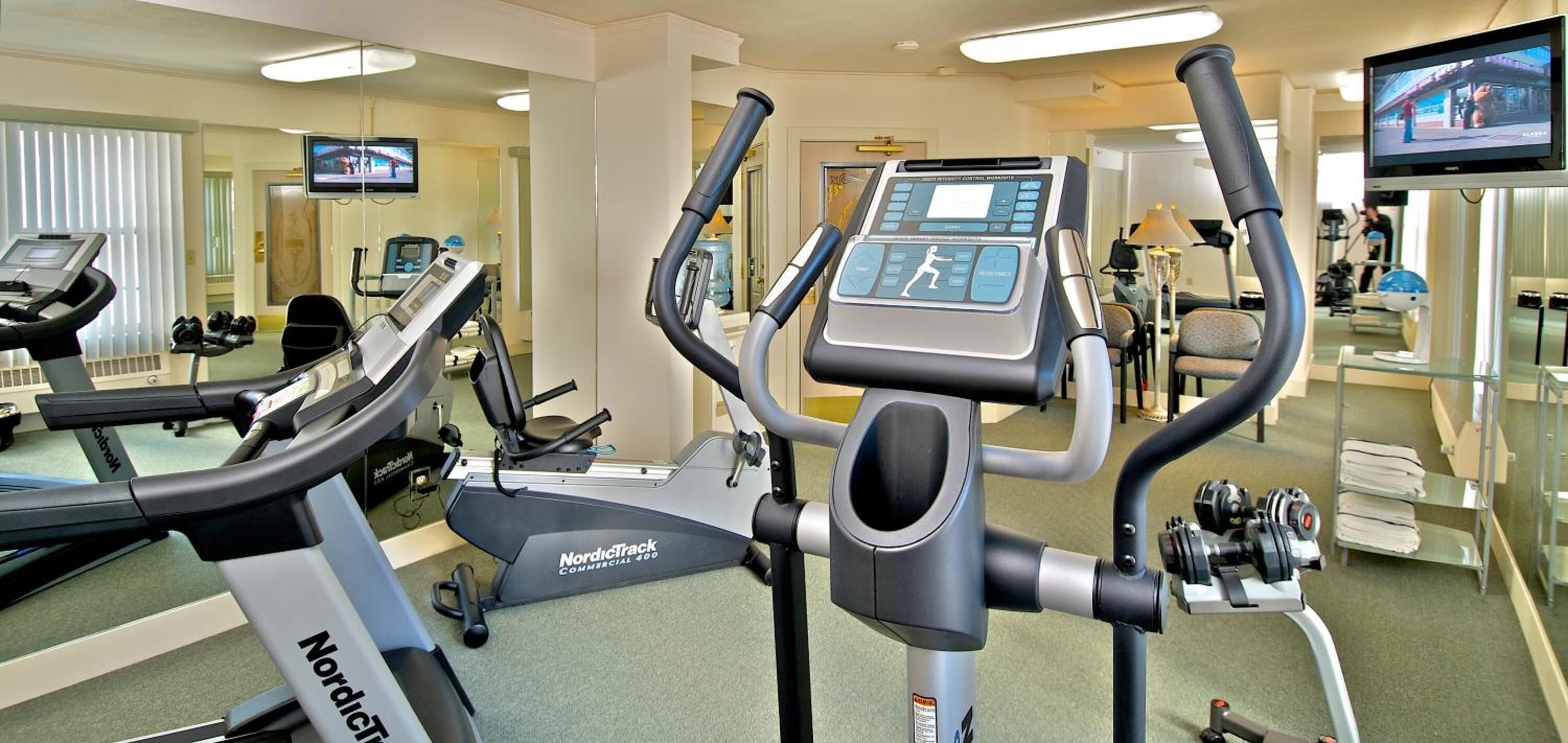 A gym with treadmills, a NordicTrack elliptical, and a TV screen.