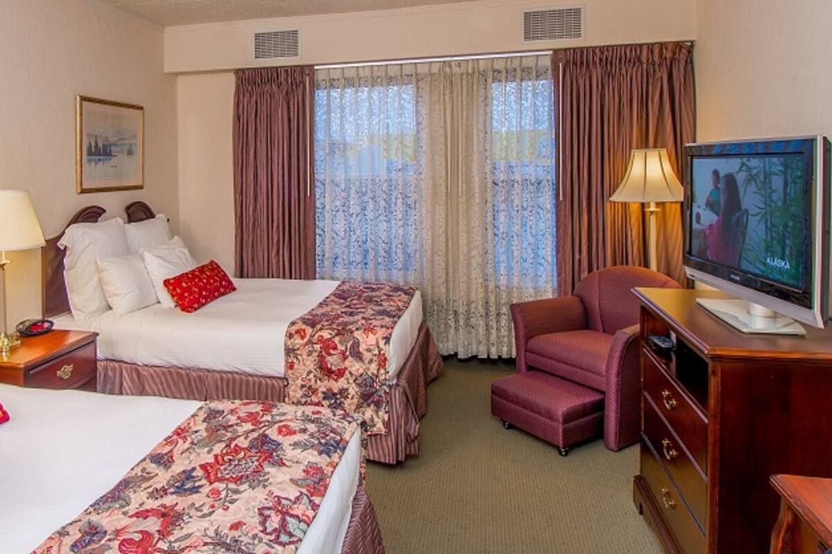 A hotel room with two beds, a television, a desk, and a chair.