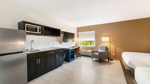 A compact hotel room with a kitchenette, a bed, a desk, and a chair.