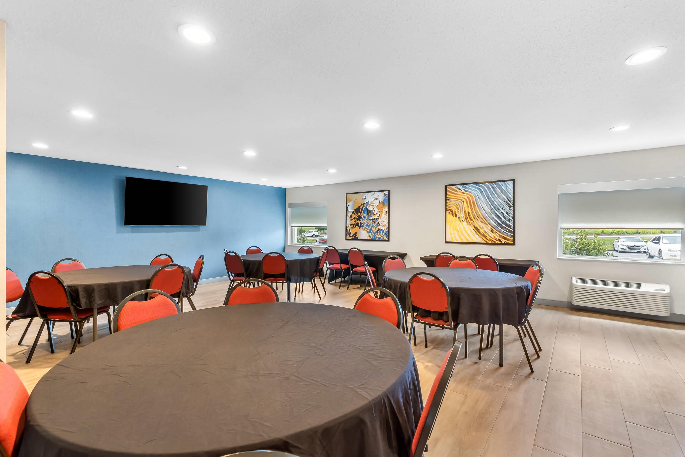 A conference room with multiple tables and chairs, a flat-screen TV mounted on the wall, and artwork on the walls.