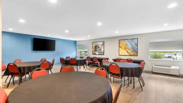 A conference room with multiple tables and chairs, a flat-screen TV mounted on the wall, and artwork on the walls.