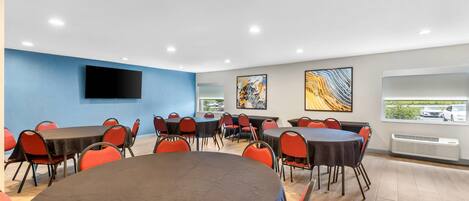 Un salón de conferencias con varias mesas y sillas, un televisor de pantalla plana en la pared y obras de arte decorando las paredes.