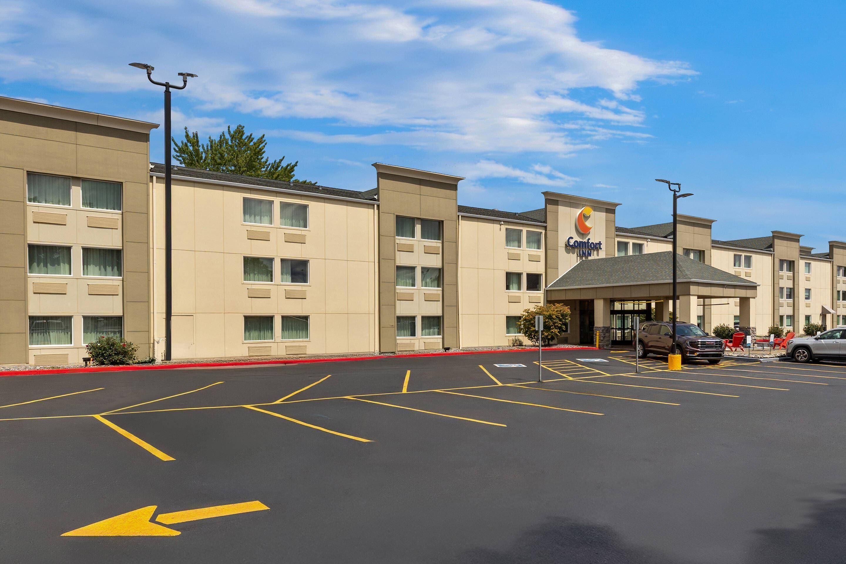 Egy szálloda, amelyhez tartozik egy parkoló, melyet irányító nyílakkal jelöltek ki, egy „Comfort Inn” tábla, és az épület homlokzata számos ablakot tartalmaz.