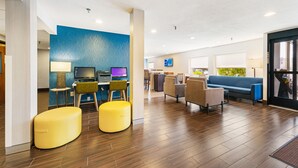 A modern hotel lobby with wooden flooring, a blue accent wall, yellow seating, and a TV.