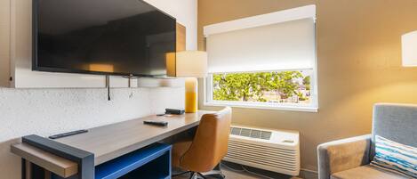 Una habitación de hotel moderna con una televisión de pantalla plana, un escritorio con silla, un ventanal con vistas y un sofá.