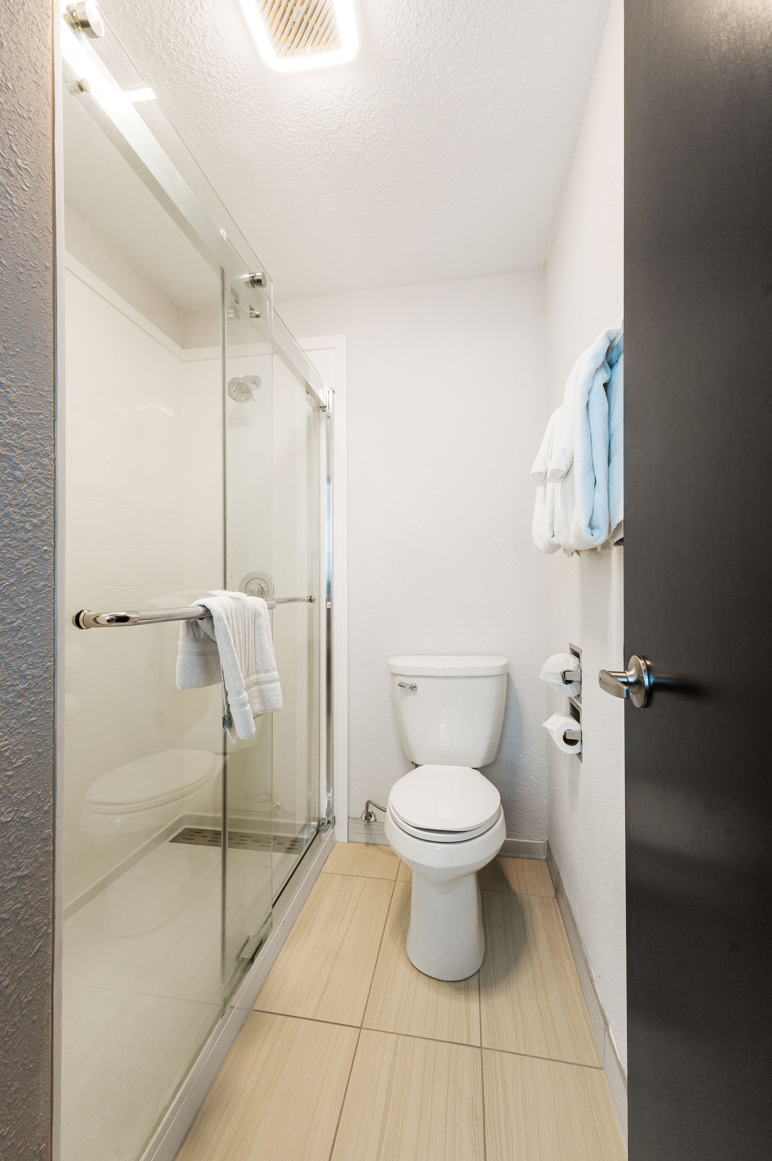 Un baño con cabina de ducha de vidrio, inodoro blanco y toallero con toallas.
