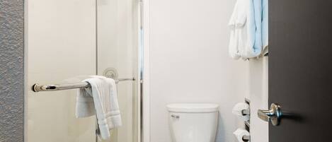Un baño con cabina de ducha de vidrio, inodoro blanco y toallero con toallas.