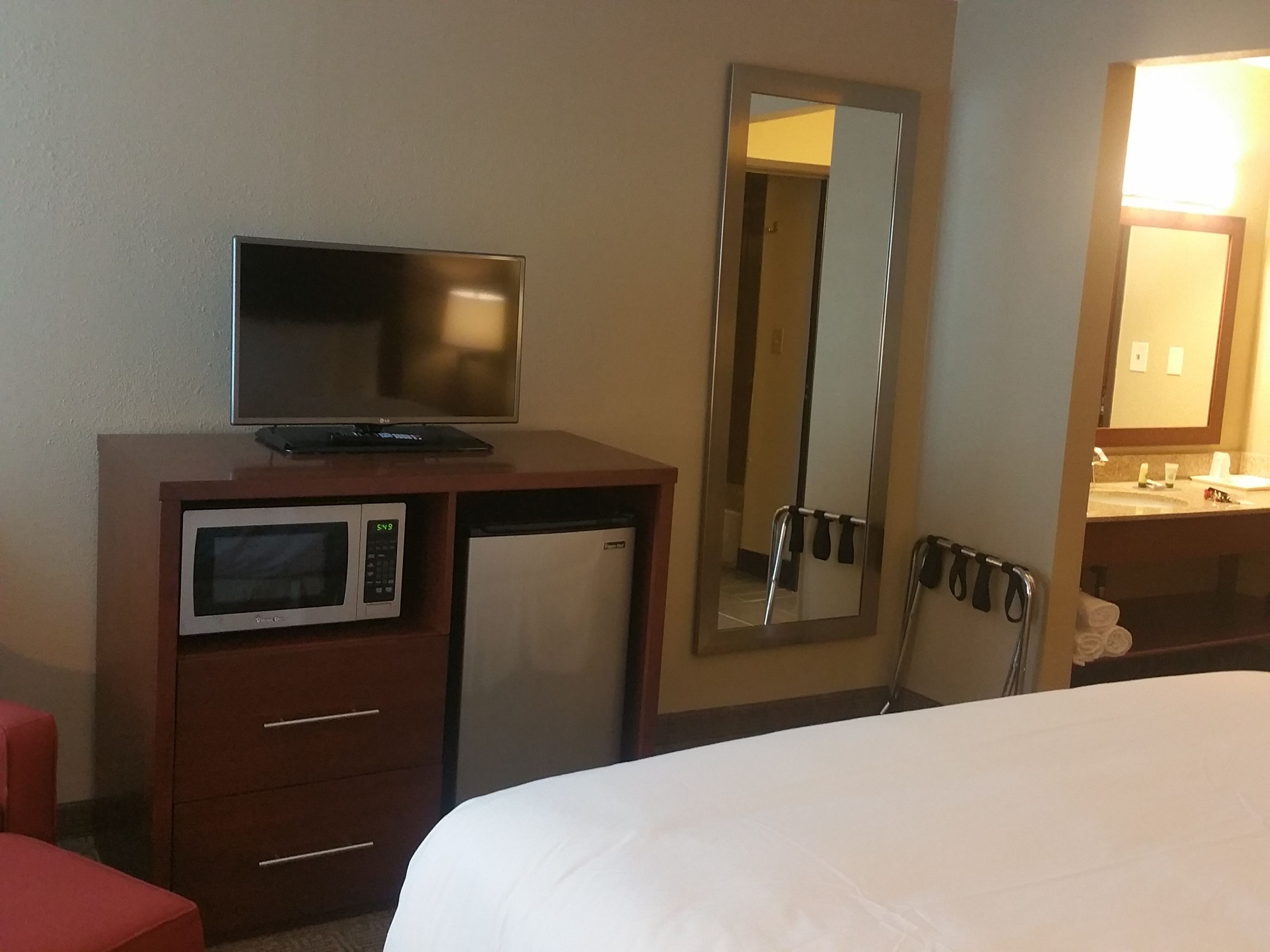 Une chambre d’hôtel équipée d’un lit, d’une télévision, d’un four à micro-ondes, d’un mini-réfrigérateur, d’un miroir et d’une salle de bain avec un lavabo et un porte-serviettes.